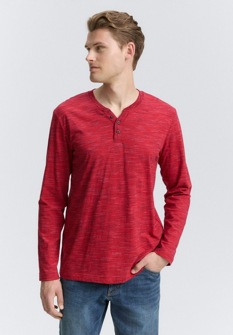 Rød langærmet Henley-skjorte med struktureret mønster, tre-knaps stolpe, rund halsudskæring, parret med blå jeans.