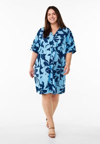 Kurzes, ärmelloses, blaues Kleid mit floralen Mustern, V-Ausschnitt und lockerem Schnitt, aus leichtem Stoff gefertigt und mit einer Mischung aus hellen und dunklen blauen Mustern.