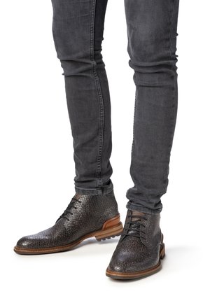 Bottes chevilles en cuir embossé serpent gris avec un talon en bois brun, associées à un jean foncé ajusté. Surface texturée avec des accents contrastants.