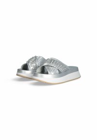 Sandales à plateforme argentées avec des brides croisées, présentant une finition texturée et des accents cloutés. Semelle épaisse blanche avec une base marron clair.