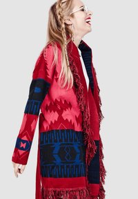 Chal rojo y azul con estampado y flecos, que presenta diseños geométricos en varias tonalidades y texturas, estilo de apertura frontal.