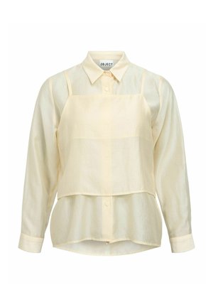 Langermet skjorte i kremfarge med knapper, med en matchende kort camisole over, på hvit bakgrunn.