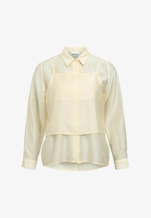 Langermet skjorte i kremfarge med knapper, med en matchende kort camisole over, på hvit bakgrunn.