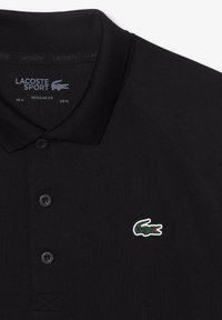 Černé sportovní polo tričko Lacoste s špičatým límcem, se třemi černými knoflíky a zeleným krokodýlem na levé hrudi. Standardní střih.