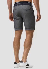 Shorts en tissu gris avec un ourlet roulé, poches arrière détaillées et une ceinture tissée bleu marine. Modèle portant des baskets blanches avec des accents noirs.