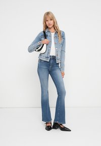 Denim jakna svetlej pranja, slim fit, s gumbnim zapiranjem in dvema žepoma na prsih, v kombinaciji s temno modrimi zvonastimi hlačami in črnimi pointed balerinkami.