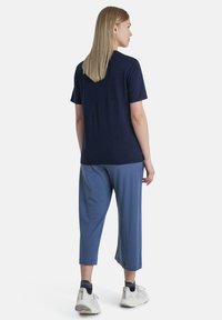 Dunkelblaues Kurzarm-T-Shirt kombiniert mit hellblauen cropped Hosen. Der Stoff scheint weich mit einem lässigen Schnitt. Tragen mit weißen und grauen Sportschuhen.