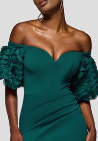 Sukienka na jedno ramię w kolorze niebieskozielonym, z falbanami na przezroczystych rękawach, dopasowanym gorsetem i głębokim dekoltem w serek. Gładki materiał o subtelnym połysku.
