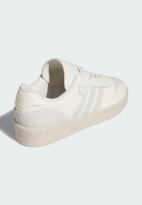 Białe niskie sneakersy z gładkiej skórzanej cholewki, trzy jasnoszare paski, wyściełany kołnierz i gruba przezroczysta gumowa podeszwa.