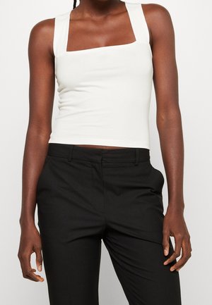 Úzké černé kalhoty spojené s bílým bezrukávovým krátkým topem s širokými ramenními popruhy a čtvercovým výstřihem.