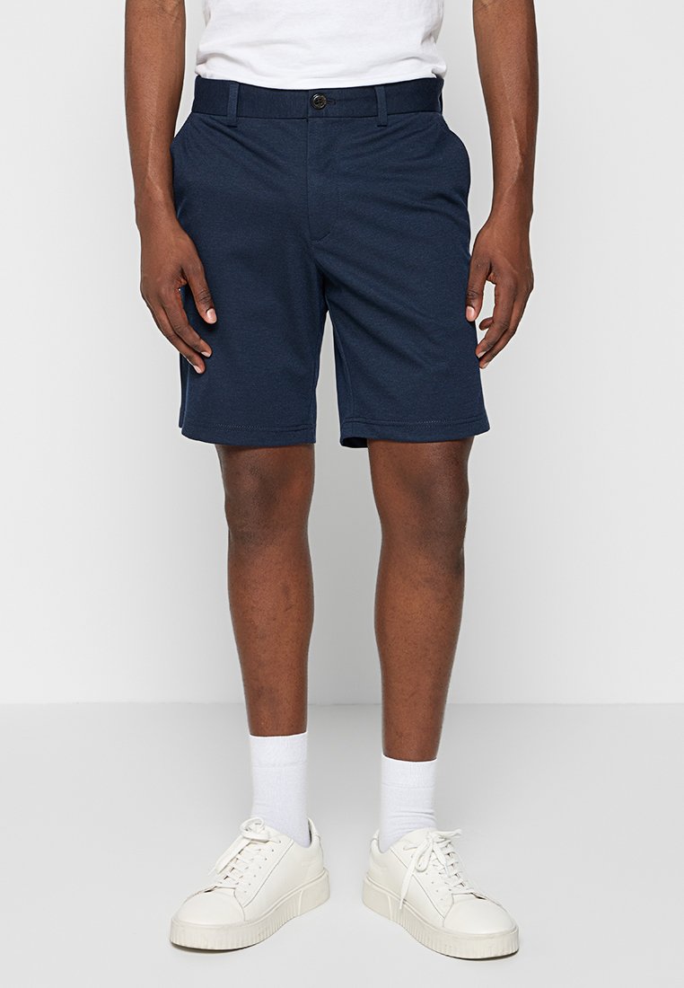 Marineblaue Shorts aus gewebtem Stoff mit flachem Vorderteil, Gürtelschlaufen und Seitentaschen. Kombinieren Sie sie mit weißen Turnschuhen und Socken.