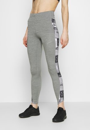 Leggings gris avec un logo Nike noir et brillant, un panneau latéral à motifs avec divers logos, et une coupe ajustée pour les vêtements de sport.