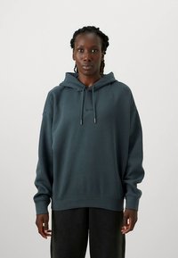 Bluza z kapturem wykonana z miękkiego, ciemnoszarego materiału. Charakteryzuje się luźnym krojem, kieszenią kangurką oraz sznurkami zakończonymi metalowymi końcówkami.