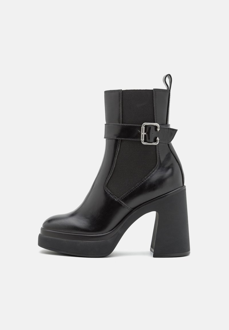 Botte cheville en cuir noir avec talon haut épais, panneau latéral élastique et bride décorative avec boucle argentée.