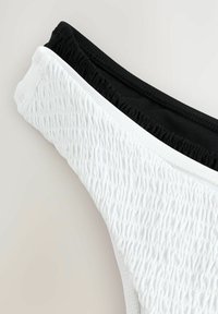 Bikini de parte inferior bicolor que presenta una textura blanca con detalles fruncidos y una cinturilla negra suave. Diseño simple con colores contrastantes.