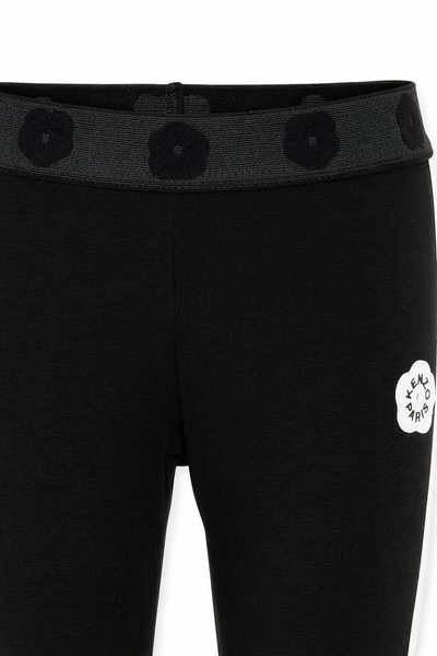 Leggings noirs avec ceinture élastique présentant des motifs floraux noirs et un logo fleur blanc avec le texte « Kenzo Paris » sur la cuisse.
