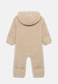 Beige, flauschiger Fleece-Einteiler für Säuglinge mit Kapuze, langen Ärmeln und Fußbündchen. Strukturierter Stoff mit sichtbaren Nähten und ohne Verzierungen.