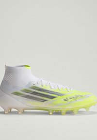 Ποδοσφαιρικό παπούτσι με λευκό και νέον κίτρινο χρώμα, με υφή στο επάνω μέρος, υψηλό σχεδιασμό στον αστράγαλο και διάφανα καρφιά στην εξωτερική σόλα.