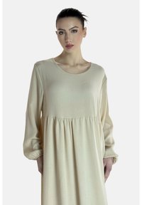 Beige jurk met lange mouwen van zachte stof, met een ronde halslijn, een geplooide taille en een vloeiende rok. Gladde textuur met subtiele vallende plooien.