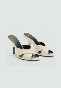 Sandalias de tacón alto abiertas en la punta de color beige con bandas cruzadas y plantilla negra. Textura suave, diseño elegante con un tacón estrecho.