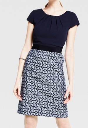 Femme portant une robe longueur genoux avec un haut uni bleu marine foncé et une jupe à motifs géométriques bleus et noirs.