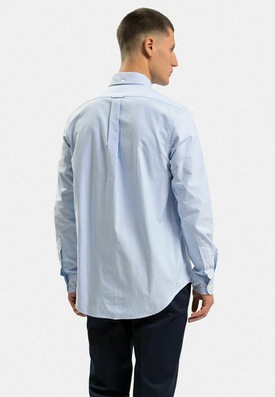Ljusblå, långärmad skjorta i cotton, med rundad nederkant, knäppte ärmslut och en enda bakveck för extra detaljer.