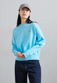 Felpa azzurra con collo e polsini a coste, caratterizzata da un piccolo logo. Abbinata a jeans in denim scuro, per un look casual.