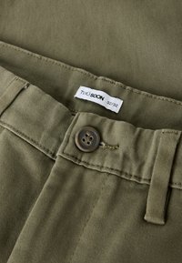 Pamučne hlače maslinasto zelene boje s gumbom za zatvaranje i tkanom etiketom na kojoj piše "TWO SOON" i veličina "32/32." Teksturirana površina, ležerni dizajn.
