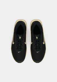 Μαύρα αθλητικά παπούτσια με υφασμένο επάνω μέρος, χρυσό λογότυπο Nike, δέσιμο με κορδόνια και μπεζ σόλα σε αντίθεση.