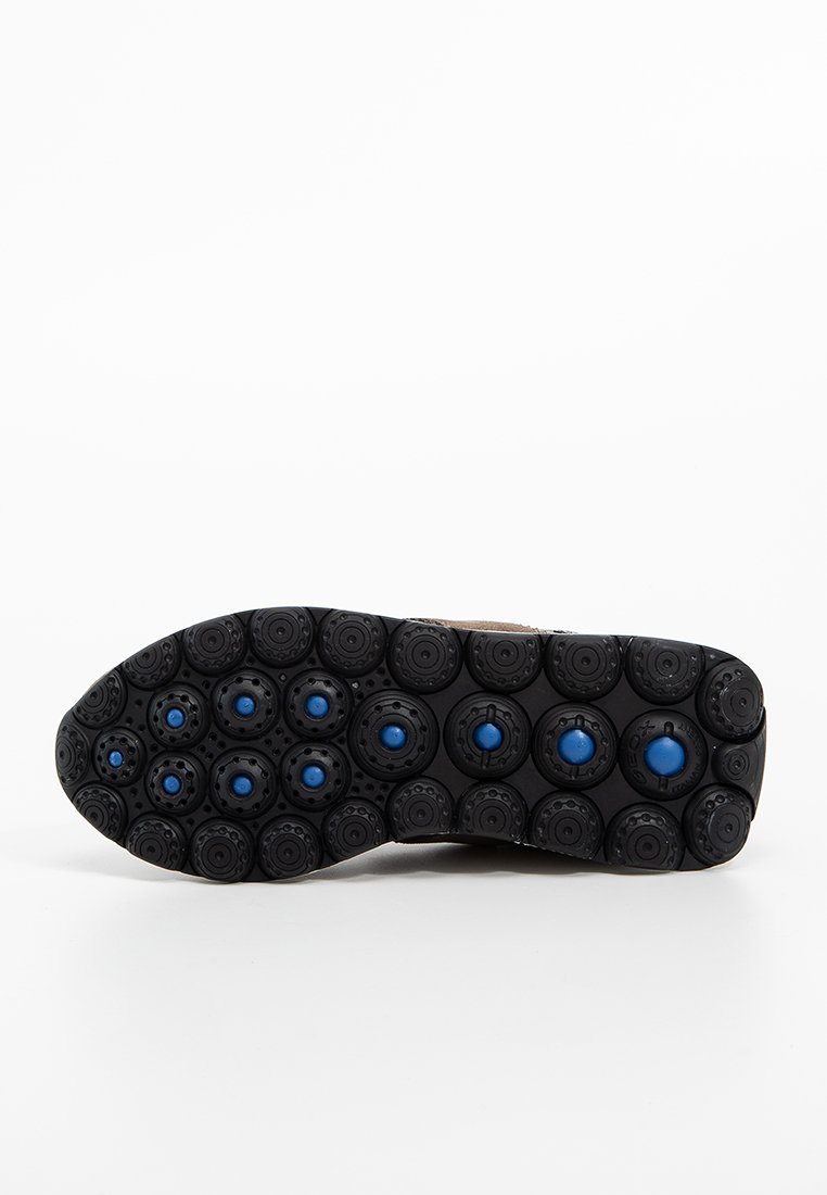 Suela de zapato con múltiples surcos circulares negros que presentan tachuelas azules distribuidas uniformemente por la parte inferior.