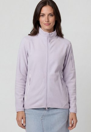 Frau trägt eine hellviolette Fleecejacke mit durchgehendem Reißverschluss und Reißverschlusstaschen an den Seiten und Ärmeln, kombiniert mit einem hellblauen Jeansrock.