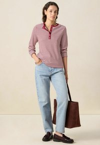Rot-weißer gestreifter Langarmshirt mit Henley-Ausschnitt, kombiniert mit hellblauen Jeans und einer braunen Wildleder-Tasche. Schwarze Slipper.