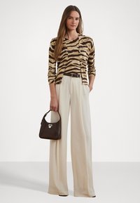 Cardigan riscado em castanho e bege por cima de uma blusa correspondente, combinado com calças plissadas de cor creme de cintura alta e uma pequena mala castanha.