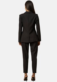 Completo nero su misura con giacca attillata e pantaloni affusolati. Tessuto liscio con bottoni ai polsini. Design classico, dettagli minimi.