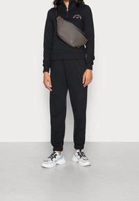 Svart zip-up hoodie med logotyp, matchande joggbyxor och vita sneakers med svarta och ljusblå accenter, plus en grå crossbody-väska.
