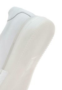 Baskets blanches avec une tige lisse et une semelle en caoutchouc translucide. Présentent un dessous plat et texturé pour l'adhérence, avec des détails de couture minimaux.