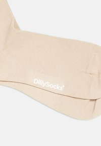 Calcetines de color beige con relieve y una textura suave, que presentan un logotipo blanco "DillySocks" cerca del puño. Diseño simple sin patrones adicionales.