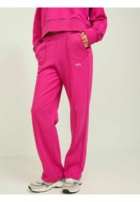 Pantalones de chándal rosa con cinturilla elástica, bolsillos laterales y detalle de logo en blanco. Hechos de una tela suave y texturizada con un corte relajado.