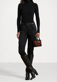 Černý žebrovaný rolák, cargo kalhoty s kapsami na zip a černé kožené vysoké boty na podpatku. Nese malou kostkovanou kabelku.