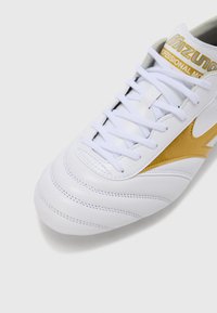 Άσπρο αθλητικό παπούτσι με υφασμένο δερμάτινο επάνω μέρος, με χρυσή λεπτομέρεια και άσπρα κορδόνια, σχεδιασμένο για άνεση και απόδοση.