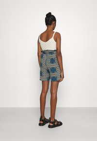 Top de tirantes tejido color crema claro con escote en V, combinado con shorts azules estampados con diseños intrincados y cinturilla elástica. Sandalias negras.