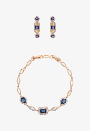 Brățară din aur rose cu zale ovale, având trei pietre pretioase albastre înconjurate de pietre transparente. Cercei cu pietre albastre și accente aurii.