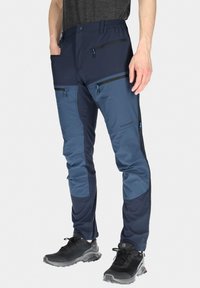 Marina och ljusblå tekniska byxor med elastisk midja, flera fickor med dragkedja och en avsmalnande passform; tillverkade av vattentåligt material.