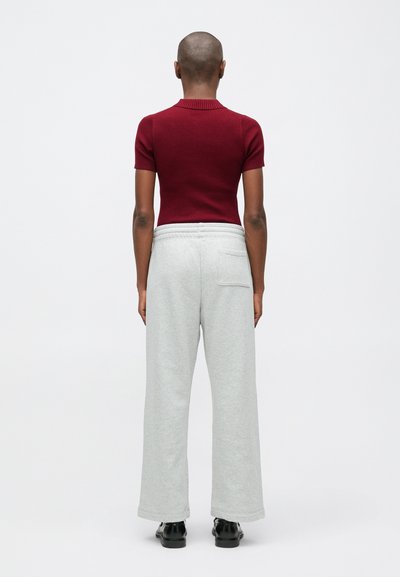 Sarkans ribots īsās piedurknes tops, kombinēts ar gaiši pelēkiem platām biksēm ar aizmugures kabatu, pabeigts ar melnām kurpēm.