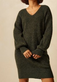 Abito maglione in verde scuro, con scollatura a V, maniche oversize, polsini a coste e una vestibilità morbida. Tessuto morbido e strutturato.
