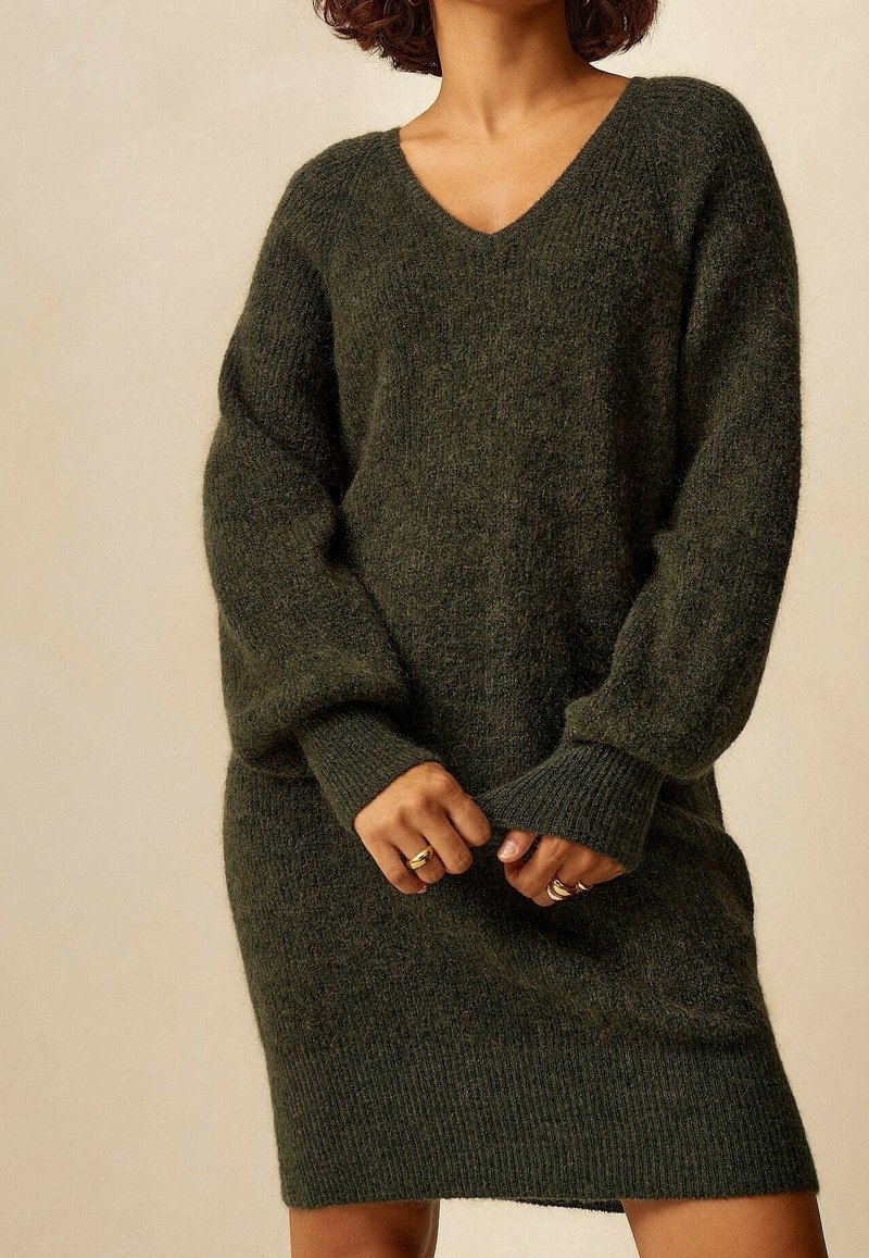 Abito maglione in verde scuro, con scollatura a V, maniche oversize, polsini a coste e una vestibilità morbida. Tessuto morbido e strutturato.