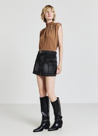 Top marrone senza maniche con scollatura arricciata, gonna in denim nera con tasche a patch e stivali neri in pelle con tacco al ginocchio.