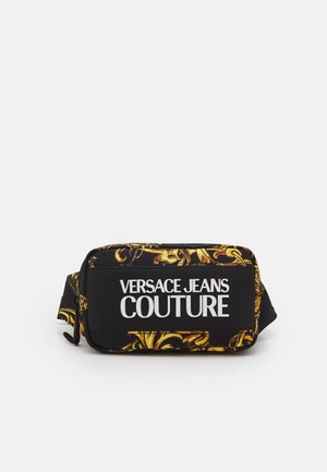 Schwarze und gold gemusterte Bauchtasche mit weißem Text ""VERSACE JEANS COUTURE"" vorne und verstellbarem Riemen auf weißem Hintergrund.