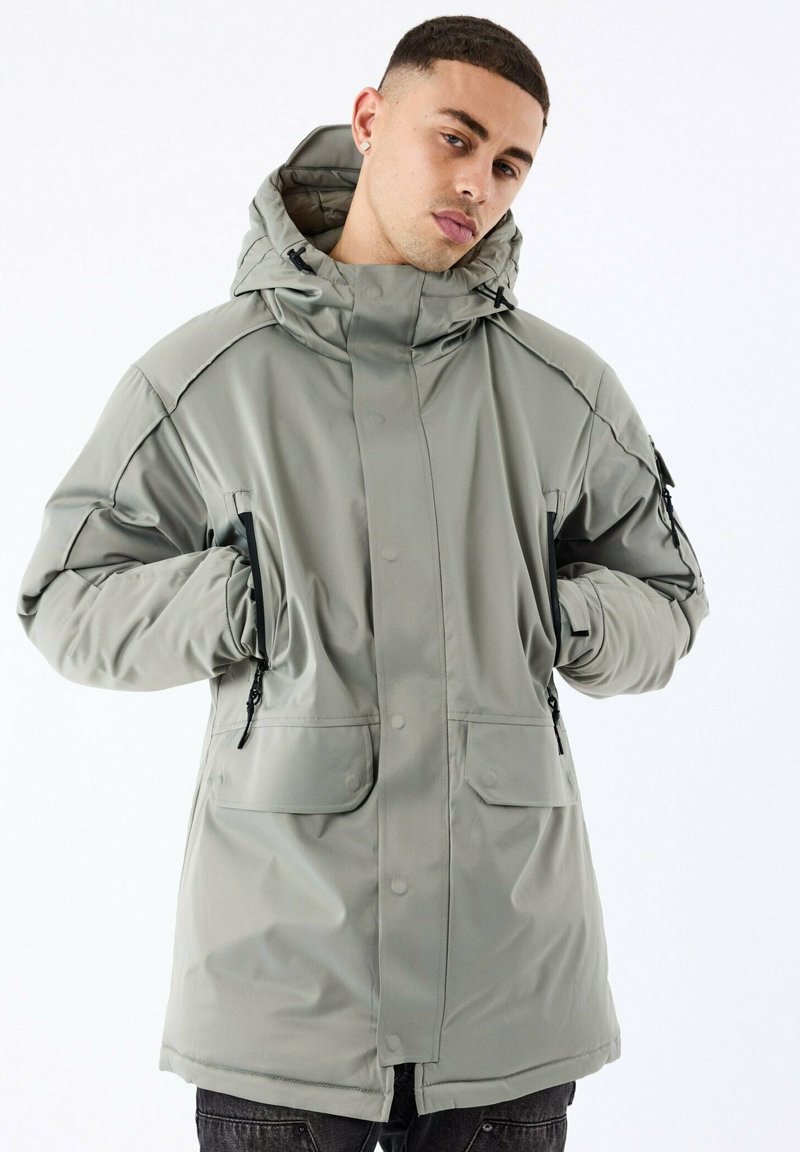Parka en toile imperméable gris clair avec capuche, dotée de fermetures à boutons-pression à l'avant, de deux grandes poches et de détails zippés sur les côtés.