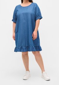Vestido de mezclilla azul, con cuello redondo, mangas cortas con volantes y un dobladillo con volante. Combina con zapatillas blancas para crear contraste.